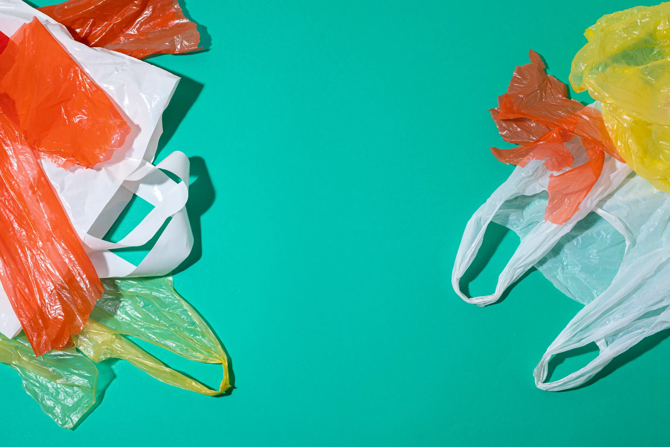 Varios tamaños de bolsas de plástico colores y tipos sobre fondo verde, incluyendo bolsas tipo camiseta y bolsas lisas